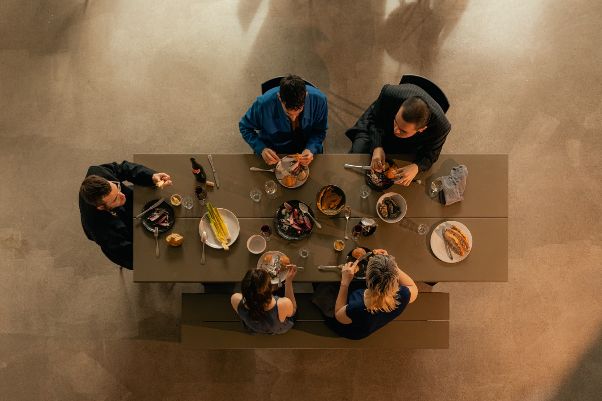 Vier gasten eten samen aan een tafel, van bovenaf gezien