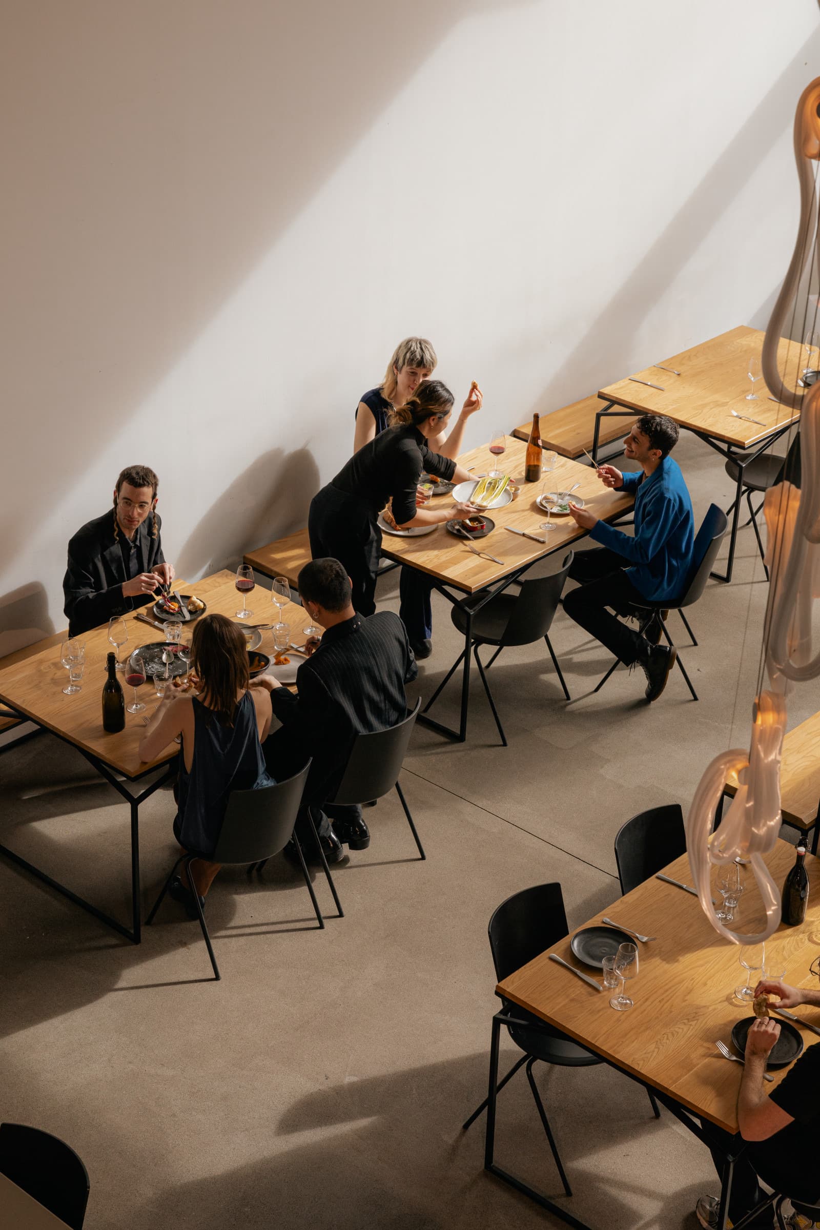 Gasten zitten aan verschillende tafels in een licht restaurant, van bovenaf gezien