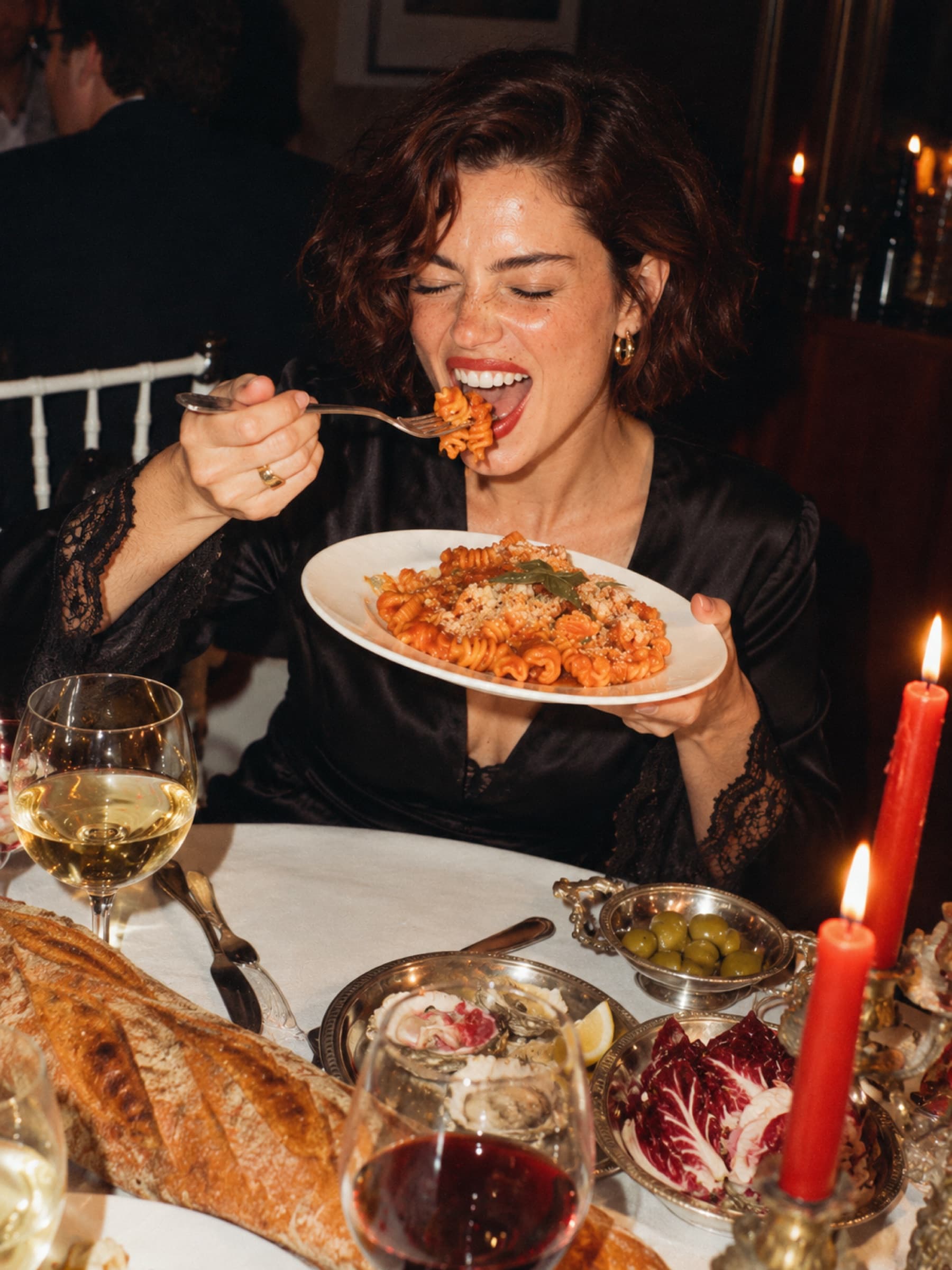 Een vrouw eet lachend pasta bij kaarslicht