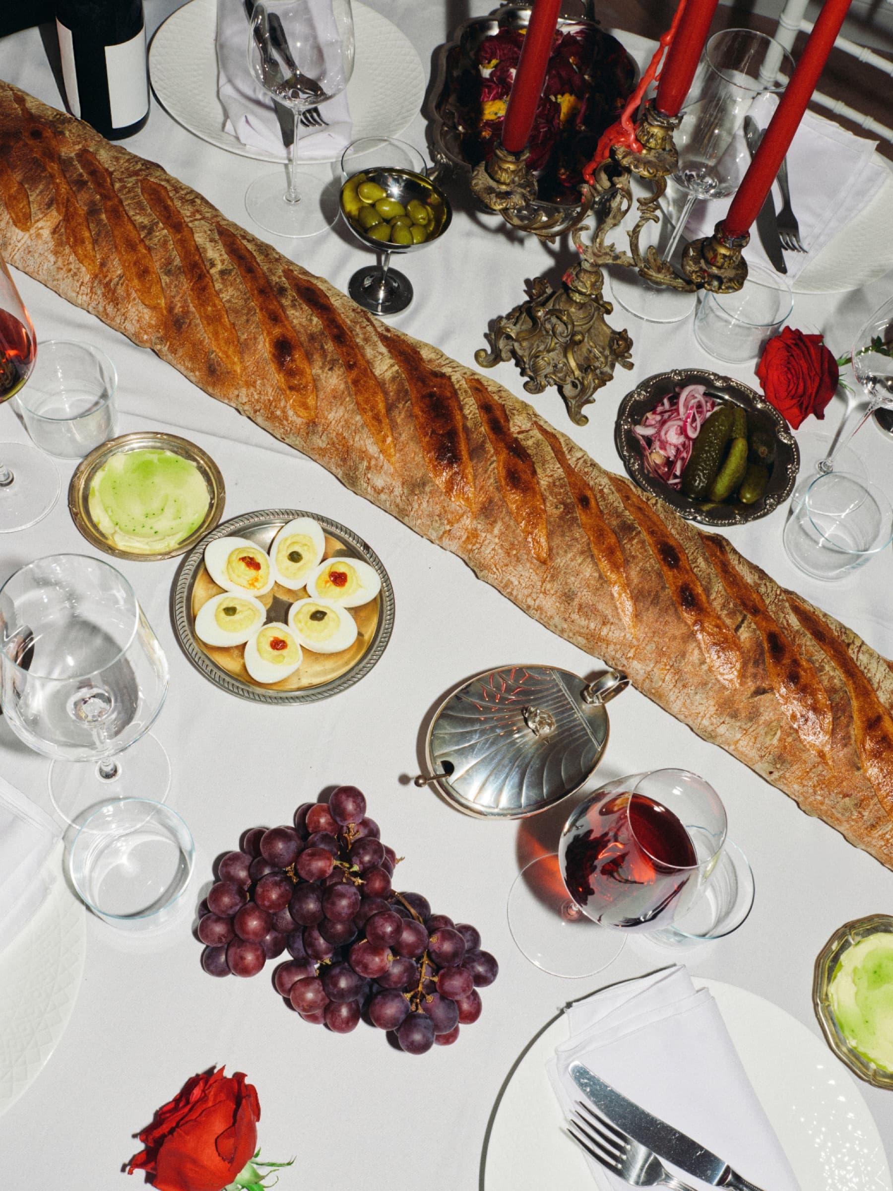 Een gedekte tafel met stokbrood, druiven en kaarsen