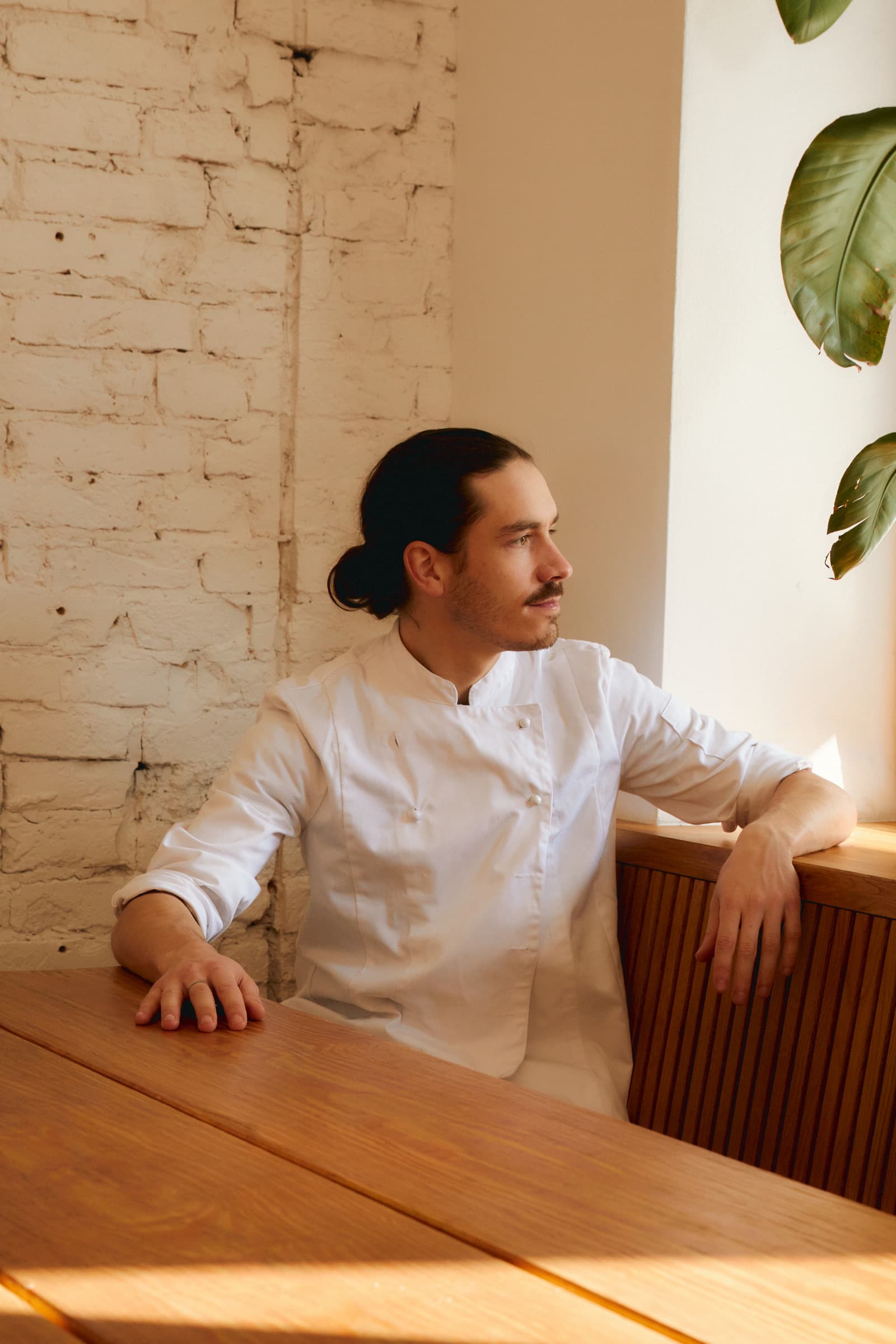 Een chef in witte jas rust uit aan een houten tafel
