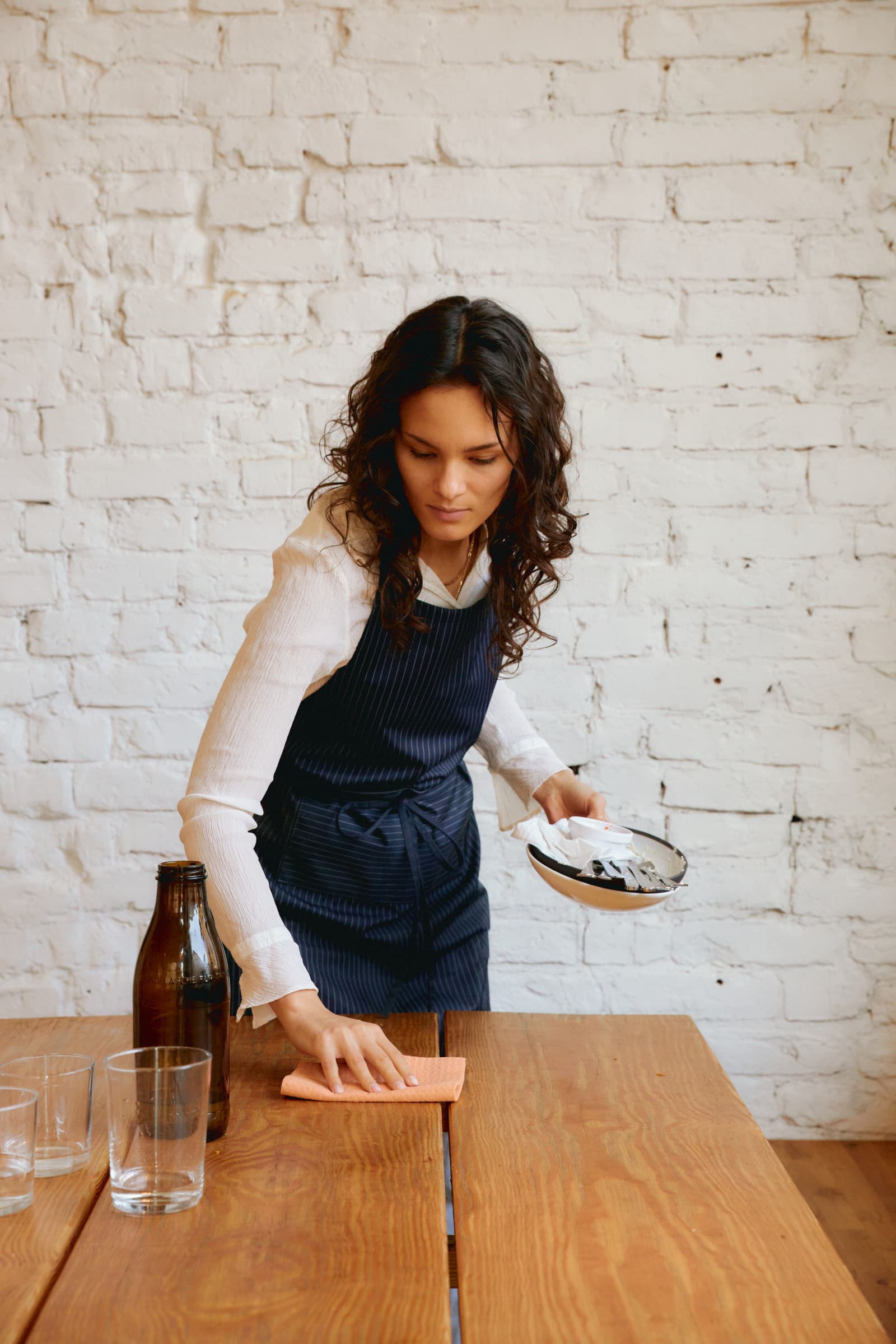 A staff member sets a table against a white brick wall