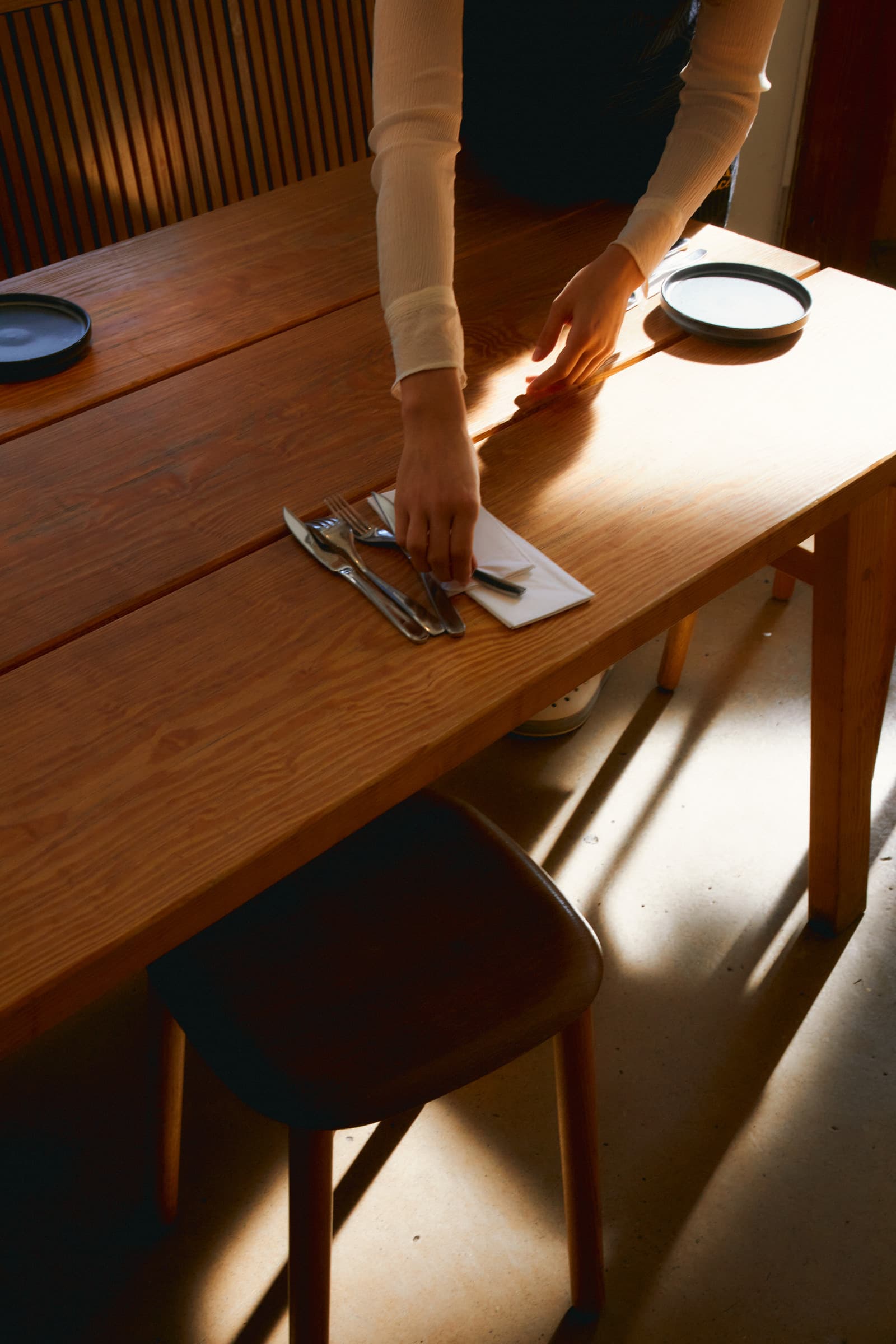 Een medewerker dekt een houten tafel in het avondlicht